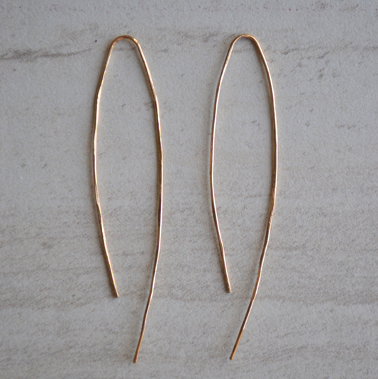 Pair of long, thin gold earrings on a light gray surface